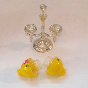 May include: A silver candle holder with three candle cups and two yellow candle shades with pink floral accents.