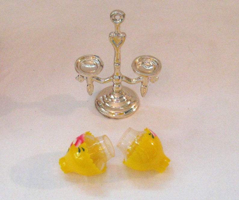 May include: A silver candle holder with three candle cups and two yellow candle shades with pink floral accents.