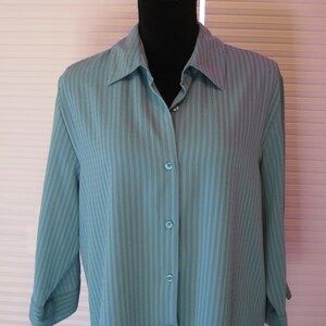 May include: A teal button-down shirt with vertical stripes. The long-sleeved shirt has a classic collar and is buttoned up the front. The shirt is displayed on a black mannequin head.