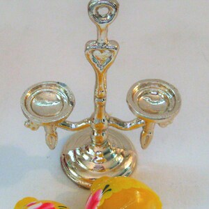 May include: Silver candle holder with a heart design and three candle cups. The candle holder is on a white surface.