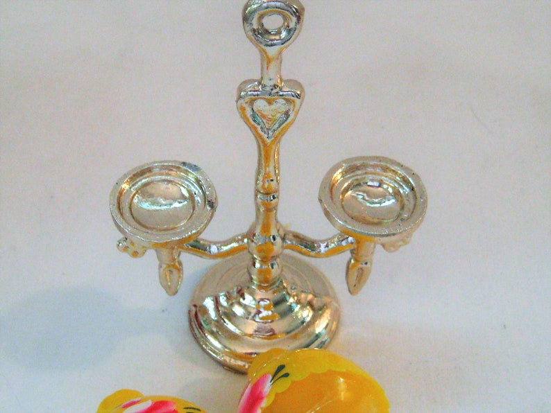 May include: Silver candle holder with a heart design and three candle cups. The candle holder is on a white surface.