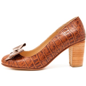 May include: Brown leather pumps with a crocodile pattern and a bow on the toe. The heels are a block style and are made of wood.