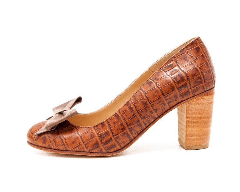 May include: Brown leather pumps with a crocodile pattern and a bow on the toe. The heels are a block style and are made of wood.