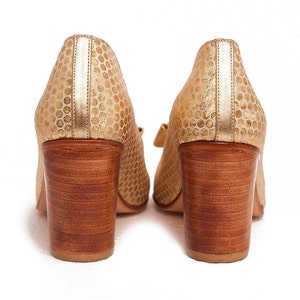 May include: A pair of gold high-heeled shoes with a polka dot pattern. The shoes have a wooden heel and a closed toe.