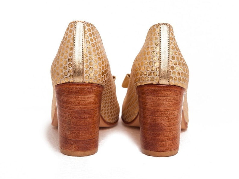 May include: A pair of gold high-heeled shoes with a polka dot pattern. The shoes have a wooden heel and a closed toe.