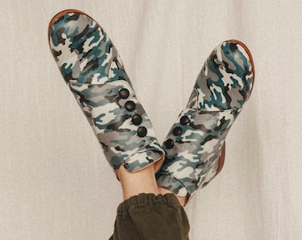 Op de afbeelding: Een paar enkellaarsjes met camouflageprint en zwarte knopen. De laarsjes zijn gemaakt van leer en hebben een ronde neus.