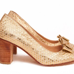 May include: A pair of gold high-heeled shoes with a textured pattern and a bow on the toe.