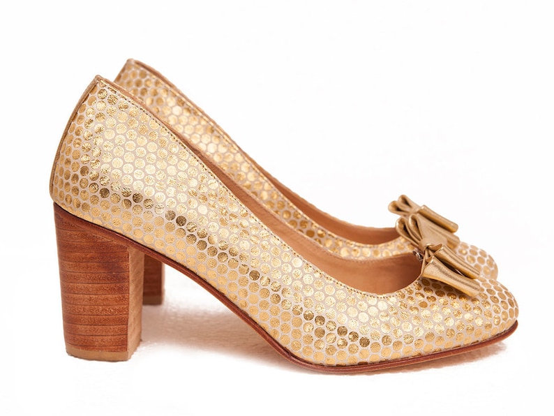 May include: A pair of gold high-heeled shoes with a textured pattern and a bow on the toe.
