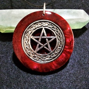 May include: A red pendant necklace featuring a silver pentagram charm encircled by a Celtic knot design.