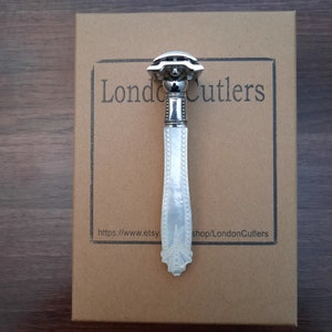 May include: A silver safety razor with a white pearl handle. The razor is on a brown cardboard box with the text 'London Cutlers' and 'https://www.etsy.shop/LondonCutlers'.