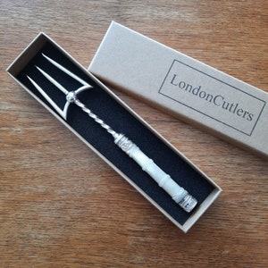 May include: A silver serving fork with a twisted handle and a white mother-of-pearl handle. The fork is in a brown box with the text "London Cutlers" printed on it.