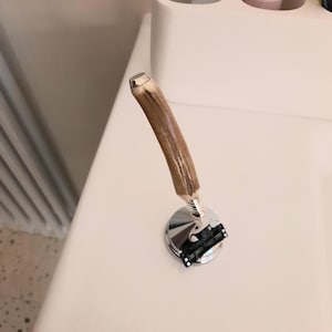 以下が含まれることがあります： 質感のある茶色の角で作られた湾曲したハンドルと、磨かれたクロムメッキの金属ヘッドを備えたカミソリ。このカミソリは、黒いプラスチック部品を使用したマルチブレードカートリッジシステムを特徴としており、銀色の金属製スプリング機構によってハンドルに接続されています。