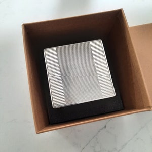 May include: A silver box with a patterned lid sits inside a brown cardboard box.