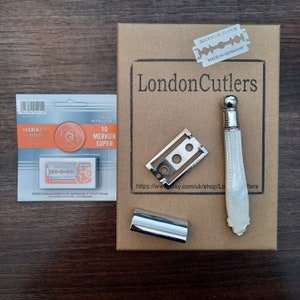 May include: A brown cardboard box with the text 'LondonCutlers' printed on it. The box contains a silver razor, a silver razor blade holder, a silver razor blade, and a pack of 10 razor blades. The razor blade pack has the text 'Merkur Solingen' and '10 Merkur Super' printed on it. The razor blade has the text 'Merkur Super' and 'Made in Germany' printed on it.