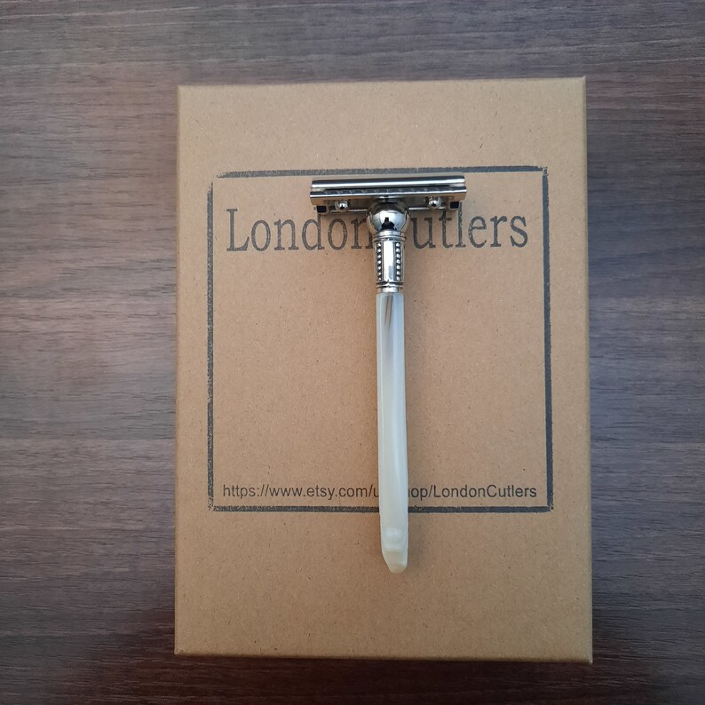May include: A silver safety razor with a white handle on a brown cardboard box. The box has the text 'London Cutlers' printed on it. The text 'https://www.etsy.com/shop/LondonCutlers' is printed on the bottom of the box.