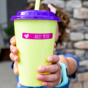 May include: A yellow reusable cup with a purple lid and a pink heart sticker that says "ADLEY MEYER" on it.