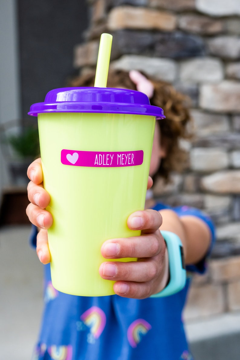 May include: A yellow reusable cup with a purple lid and a pink heart sticker that says "ADLEY MEYER" on it.