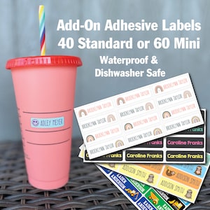 May include: A set of colorful waterproof and dishwasher safe adhesive labels with various names and designs. The labels are shown on a pink tumbler with a straw and a stack of labels with rainbow, sloth, and construction vehicle designs.
