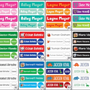 K&ouml;nnte beinhalten: Eine Sammlung personalisierter Namensetiketten in verschiedenen Farben, darunter Rosa, T&uuml;rkis, Rot und Gr&uuml;n. Jedes Etikett enth&auml;lt einen Namen und eine kleine Grafik, wie z. B. einen Fu&szlig;ball oder einen Dinosaurier. Die Etiketten sind rechteckig und oval.