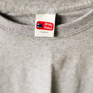 Puede incluir: Una etiqueta blanca desprendible con texto rojo que dice "Brody Matsui" y un peque&ntilde;o gr&aacute;fico de tren azul. La etiqueta dice "Tearaway" debajo del texto.