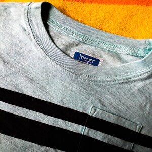 May include: A light blue striped t-shirt with a pocket and a blue label that says "Meyer" on it.
