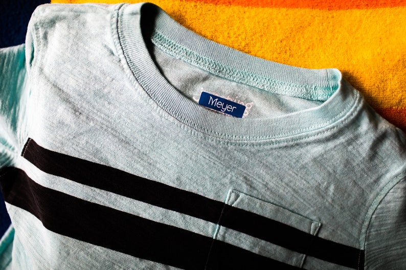 May include: A light blue striped t-shirt with a pocket and a blue label that says "Meyer" on it.