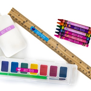 May include: A set of school supplies with personalized labels featuring the name "Adley Meyer". The set includes a bottle of white glue, a wooden ruler, a set of crayons, and a watercolor paint set.
