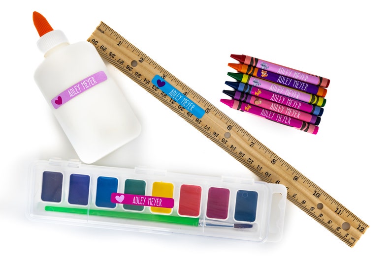 May include: A set of school supplies with personalized labels featuring the name "Adley Meyer". The set includes a bottle of white glue, a wooden ruler, a set of crayons, and a watercolor paint set.
