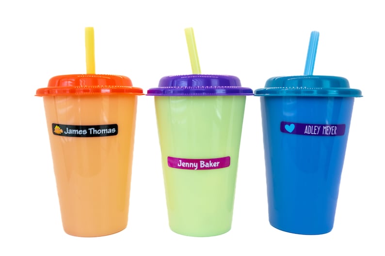 May include: Three colorful plastic cups with straws and personalized labels. The cups are orange, green, and blue. The labels read "James Thomas", "Jenny Baker", and "Adley Meyer".