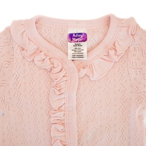 Puede incluir: Un c&aacute;rdigan rosa para beb&eacute; con cuello de volantes y cierre de botones. El c&aacute;rdigan est&aacute; hecho de un tejido de punto delicado y tiene una etiqueta que dice "Addley Meyer Boutique Knits".