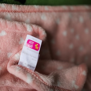 Puede incluir: Manta de forro polar rosa con estrellas blancas y una etiqueta blanca que dice "Avery Award" con un logotipo rosa y naranja de un ciervo.