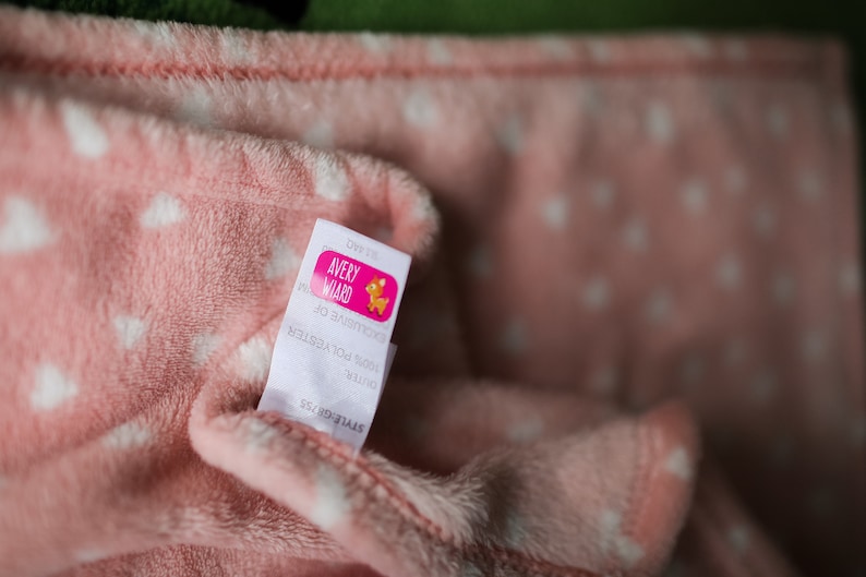 Puede incluir: Manta de forro polar rosa con estrellas blancas y una etiqueta blanca que dice "Avery Award" con un logotipo rosa y naranja de un ciervo.