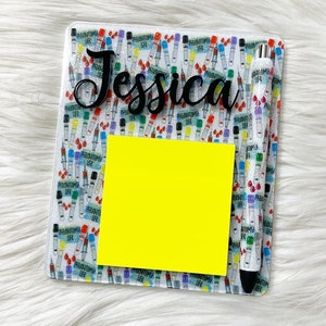 May include: A clear acrylic desk organizer with a colorful pattern of test tubes and the word "PHLEBOTOMIA LAB" printed on them. The organizer has a yellow sticky note and a black pen with a white and red pattern. The name "Jessica" is printed in black on the top of the organizer.