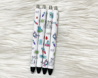May include: Four white pens with black tips, decorated with colorful science-themed illustrations. The designs include microscopes, beakers, test tubes, and lab coats. The pens are arranged vertically against a white, fluffy background.