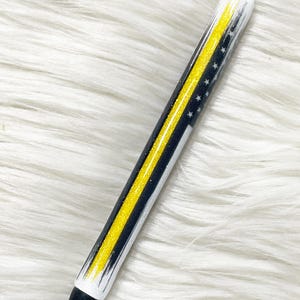 May include: A black and white pen with a yellow stripe and stars. The pen has a silver tip and a black tip. The pen is decorated with glitter.