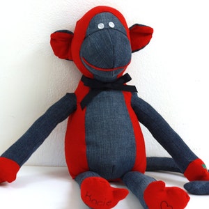 May include: A red and blue denim monkey plush toy with black eyes and a black bow tie. The toy is sitting on a white surface and has the name "Kacie" embroidered on one foot.