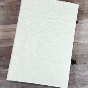 May include: A white journal with a textured cover featuring a repeating pattern of embossed flowers. The cover has a slightly off-white color.