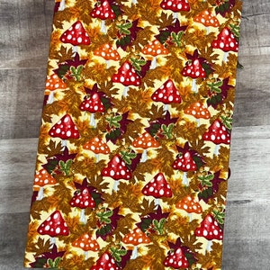 May include: A yellow fabric notebook cover with a pattern of red and white mushrooms and brown leaves.