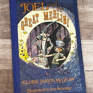 May include: A blue book cover with the title "JOEL and the GREAT MERLINI" in orange lettering. The cover features an illustration of a magician with a wand and a young boy in a top hat. The text "by ELOISE JARVIS McGRAW" and "Illustrated by Jim Arnosky" is also on the cover.