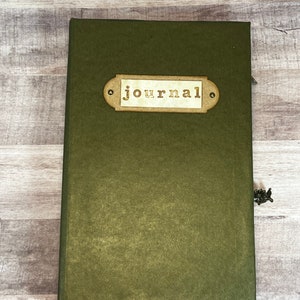 May include: A dark green journal with a brown label that says "journal" in a vintage font.