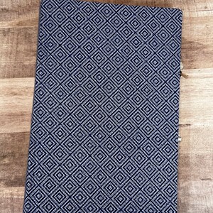May include: A dark blue notebook with a white geometric pattern. The notebook has a textured cover and a simple design.
