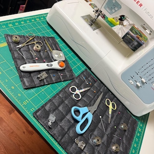 May include: A white Singer Futura sewing machine with a green cutting mat and two black fabric organizers filled with sewing supplies, including scissors, needles, thread spools, and a seam ripper.