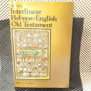 May include: A gold-coloured book titled "The NIV Interlinear Hebrew-English Old Testament." The cover features a colourful illustration with Hebrew text and circular designs. The book is edited by John R. Kohlenberger III, Vol. 1, Gen.-Deut.
