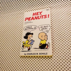 May include: A vintage comic book cover featuring Charlie Brown and Snoopy from the Peanuts comic strip. The cover is yellow with red and black text that reads "Hey, Peanuts!" and "Selected Cartoons from More Peanuts Vol. 2". The cover features a cartoon illustration of Charlie Brown and Snoopy.