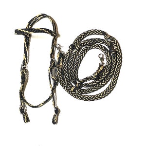 May include: Black and gold braided leather horse halter and reins set. The halter has a simple design with a single buckle on the noseband. The reins are long and braided with a decorative knot at the end.