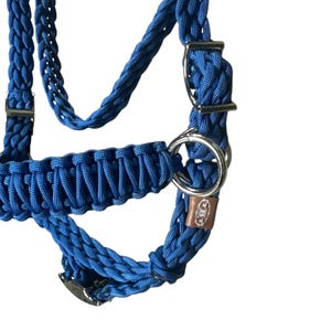 May include: A blue braided rope halter with silver hardware and a brown leather tag with the text "HKM" on it.
