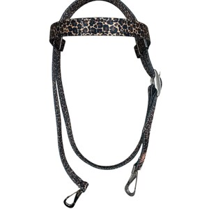 May include: A leopard print horse halter with a padded crown and cheek pieces. The halter features silver-colored metal hardware, including a buckle and two snap hooks. The pattern is a mix of black and tan spots.