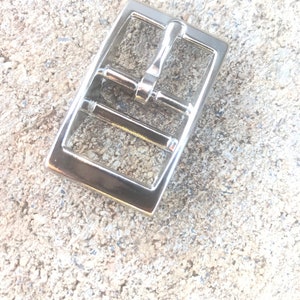 May include: Silver metal buckle with a rectangular shape and a sliding clasp.