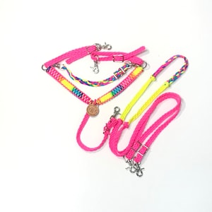 May include: A set of pink and yellow braided horse reins with a leather concho. The reins have silver snap hooks and are made of a soft, durable material.