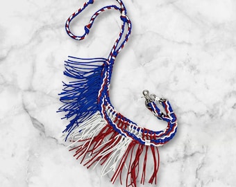 May include: A red, white, and blue braided rope halter with fringe. The halter is made of a thick, durable rope and has a silver metal snap.